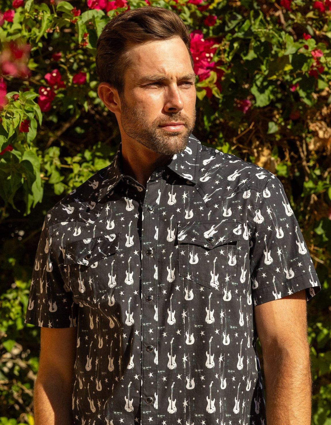 Man wearing a black shirt with white guitar pattern against a floral background